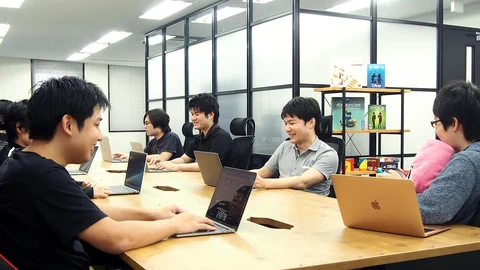 Mehrere junge Japaner sitzen an einem Konferenztisch, jeder arbeitet an einem Laptop vor sich