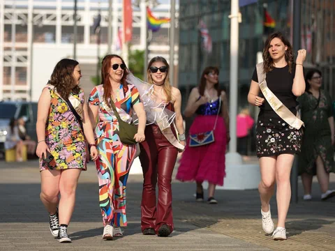 Junge Frauen in bunten Kleidern flanieren durch eine Strasse.