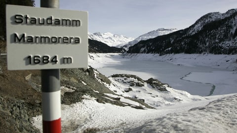 Ein gefrorener Stausee mit Schild Staudamm Marmorera