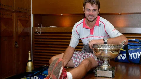 Wawrinka sitzt neben seinem Pokal auf einem Tisch.