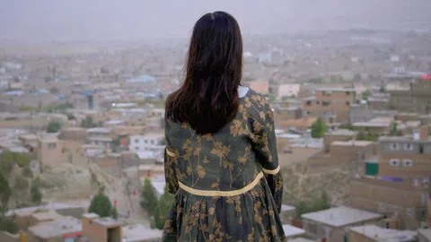 Eine Frau steht mit dem Rückern zur Kamera und überblickt eine Stadt in Afghanistan.