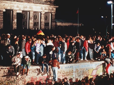 Die Berliner Mauer am Brandenburger Tor in der Nacht, die Menschen treffen sich auf de Mauer und feiern, November 1989