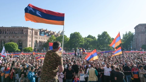 Mann in Militäruniform vor Menschenmenge mit armenischen Flaggen.