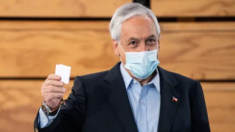 Chiles Präsident Sebastián Piñera trägt eine Maske und hält seinen Stimmzettel hoch.