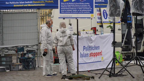 Eine Polizstin und ein Polizist sichern Spuren vor einem Stand auf der Strasse.