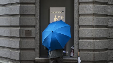 Ein Kunde mit Regenschirm an einem Bancomat der Credit Suisse.