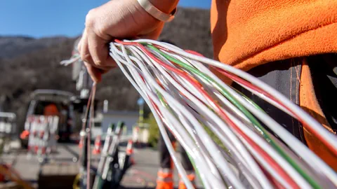 Arbeiter hält Bündel bunter Kabel vor Baustellenhintergrund.