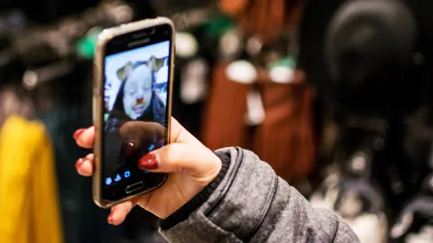 Eine junge Frau blickt auf ein Smartphone mit FIlter-Selfie.