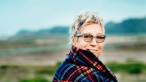 Eine blonde Frau mit Brille in der Natur.