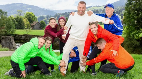 8 Menschen in Sportkleidung halten einen Mann spielerisch fest.