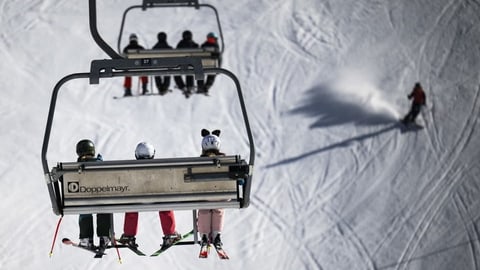 Skifahrer auf Sessellift und Piste im Hintergrund.