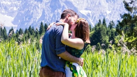 Ein Mann und eine Frau küssen sich auf einer Blumenwiese.