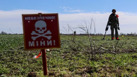 Mann mit Metalldetektor nahe Warnschild für Minen auf Feld.