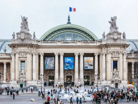 Der Grand Palais in Paris mit der französischen Flagge auf dem Dach und Menschen auf dem Vorplatz.