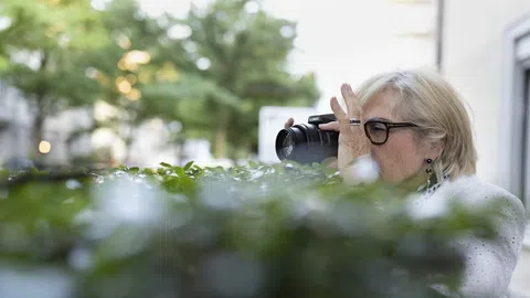 Frau mit Fotoapparat versteckt sich hinter einem Gebüsch