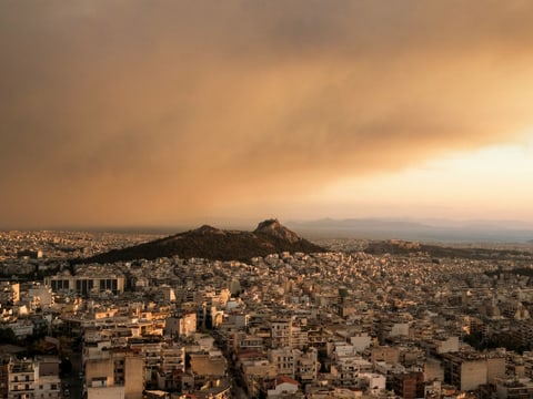 Stadtansicht von Athen mit Hügel und bewölktem Himmel.