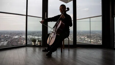 Ein Mann spielt Cello, hinter ihm die Aussicht über eine Stadt.