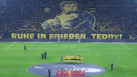 Fussballspiel mit grosser Gedenkbanner, gelbe und rote Mannschaften.