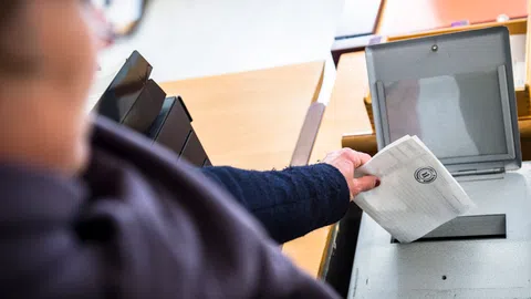 Eine Frau wirft ihre Wahlunterlagen in eine Wahlurne.