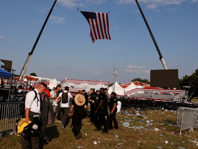 Menschen versammeln sich unter aufgehisster amerikanischer Flagge bei einer Veranstaltung im Freien.