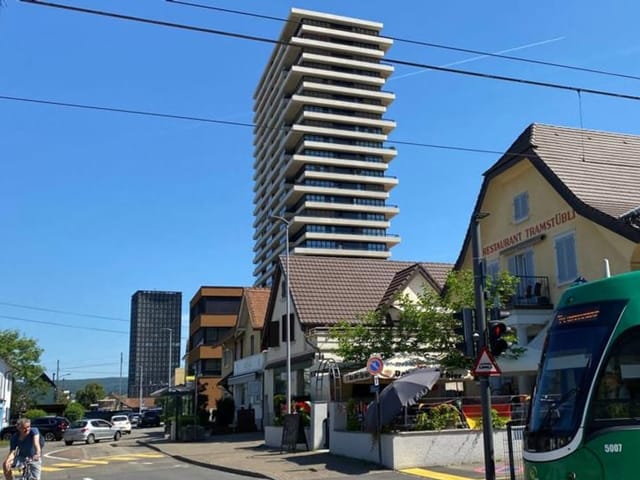 Ein Turm steht neben kleineren Wohnhäusern.