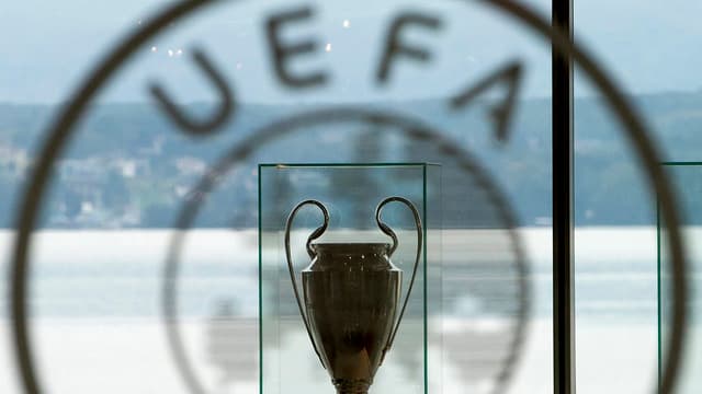 Symbolbild: Uefa-Logo auf einer Scheibe, davor ein Pokal, im Hintergrund Sicht auf den Genfersee.