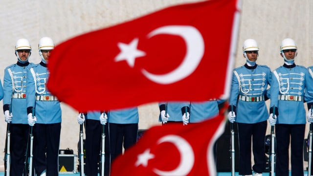 Eine Reihe von Gardisten in hellblauer Uniform steht stramm vor einer türkischen Flagge.