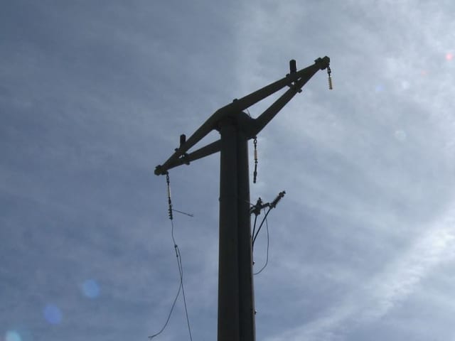 Hochspannungsmasten aus Beton mit heruntergerissenen Isolatoren und Kabel.