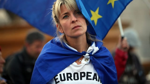 Eine Frau in weissem T-Shirt mit Überschrift «European», vor einer EU-Flagge.