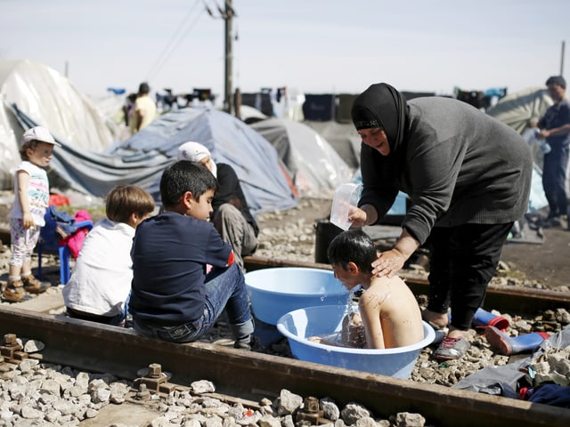 Eine Frau wäscht ein Kind, das in einer Plastikschale sitzt auf einer Schiene in Idomeni. Darum herum versammelt sind weitere Kinder. (reuters)