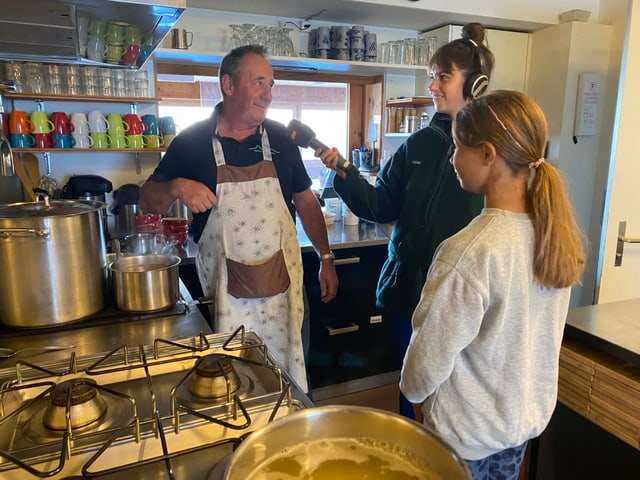 Küchenchef und Koch Christian beantwortet für SRF, Fragen über seine Aufgaben in der Berghütte. Sophie hört gespannt zu.