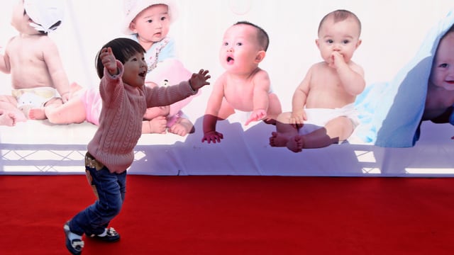 Ein chinesisches Kind vor einer Bilderwand mit Babys