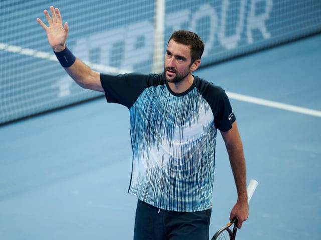 Männlicher Tennisspieler winkt mit Schläger auf dem Platz.