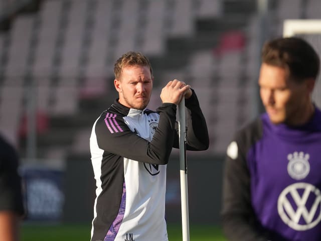 Mann im Trainingsanzug steht auf einem Fussballfeld.