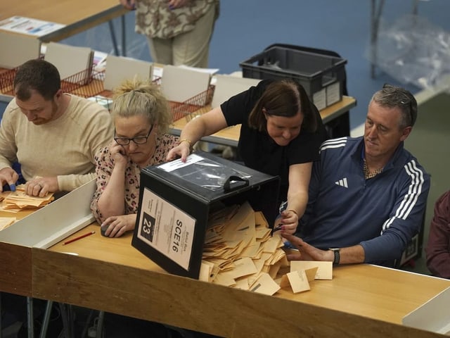 Menschen zählen Wahlstimmen an einem Tisch.