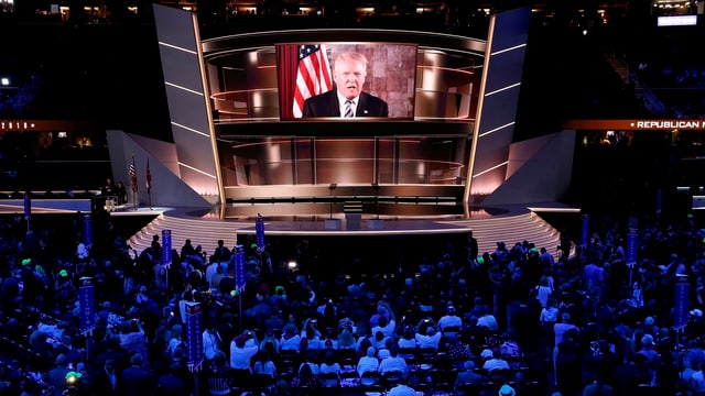 Menschen schauen auf eine Leinwand, auf der Donald Trump zu sehen ist.