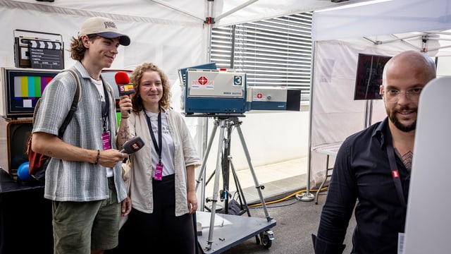 Ein junger Mann und eine junge Frau lassen sich mit zwei alten Mikros vor alten TV- und Radiogeräten fotografieren.