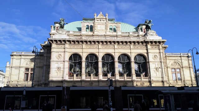 Ein grosses Operngebäude mit Bogenfenstern, grosser Kuppel und Pferdestatuen. 