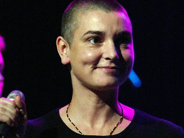 Sinéad O'Connor auf einer Bühne und hält ein Mikrofon in der rechten Hand. 