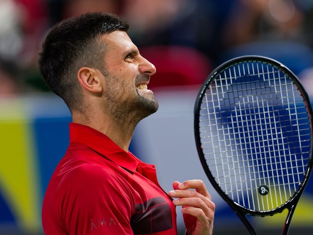 Tennisspieler mit rotem Hemd und Schläger auf dem Platz.