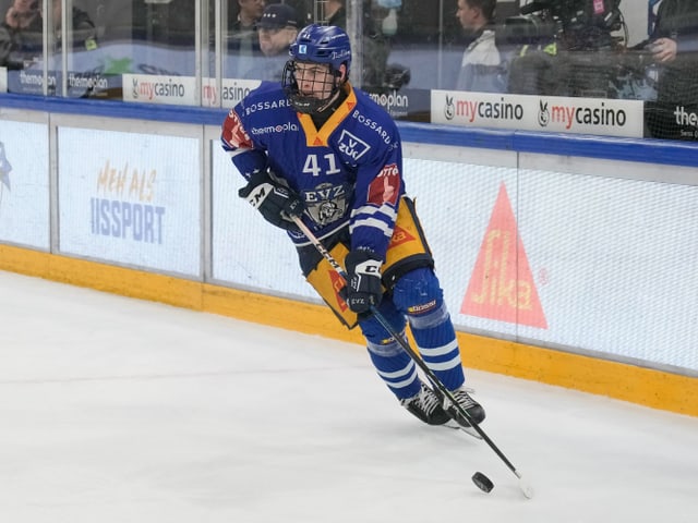 Eishockeyspieler im blauen Trikot mit Puck auf dem Eis.