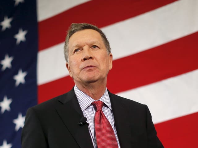 John Kasich vor einer grossen Flagge der USA.