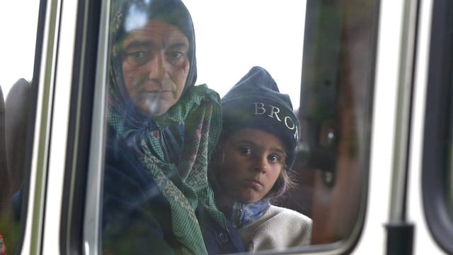 Eine Frau mit Kopftuch und ein Kind mit Strickmütze hinter einer Scheibe eines Buses.