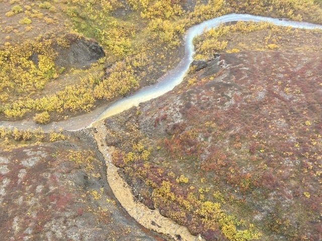 Ein Fluss und ein Bach mit orange-Färbung fliessen durch eine Landschaft.