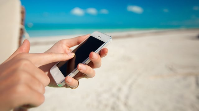 Frau am Strand tippt etwas in ihr Smartphone ein.