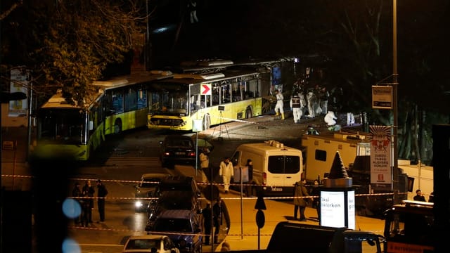 Männer in weissen Anzügen an zerstörten Bussen. 