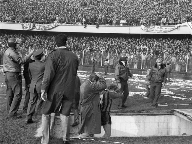 Menschenmenge im Stadion, Sicherheitskräfte im Vordergrund.