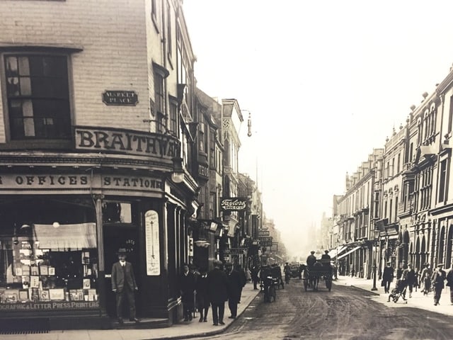 Historische Strassenszene mit Geschäften und Pferdekutschen.