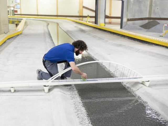 Mann arbeitet an einem Modell einer Brücke über einem kleinen künstlichen Fluss.