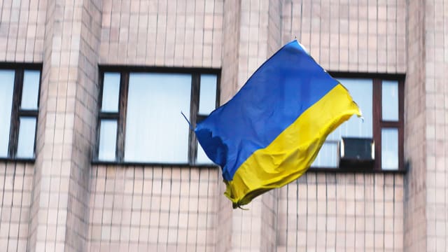 Die ukrainische Flagge in der Luft vor einem Gebäude.